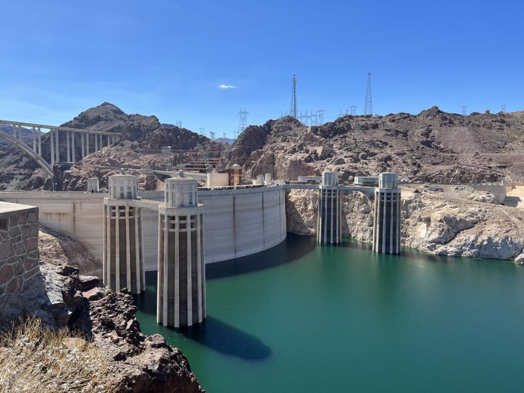 Scenic view of Hoover Dam spanning the Colorado River between Nevada and Arizona, with turquoise reservoir water and desert mountains under a clear blue sky.