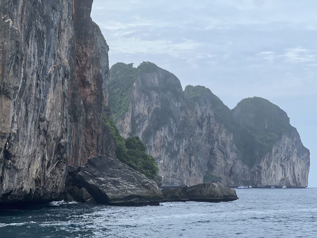 Dramatic limestone cliffs and light blue waters of Phi Phi Islands, Thailand, with boats anchored near the shore.