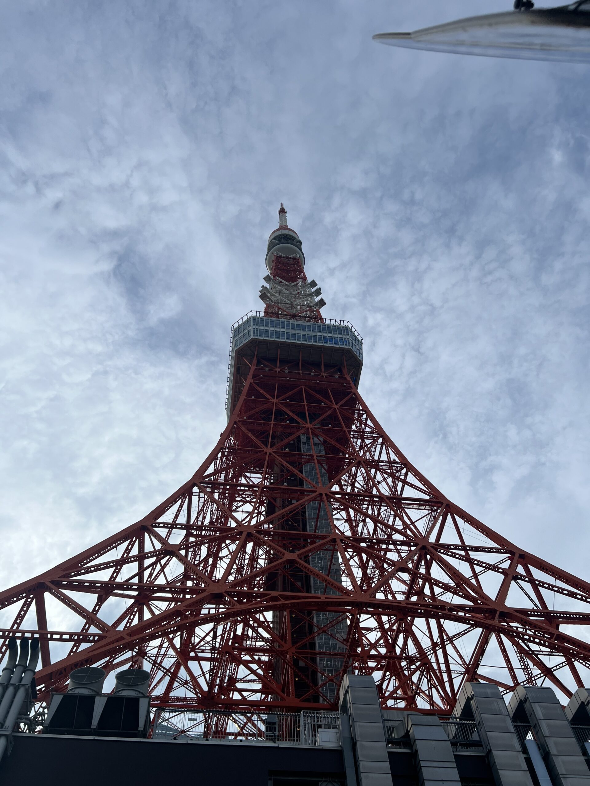 Upward view of the iconic red Tokyo Tower against a cloudy blue sky in Japan.
