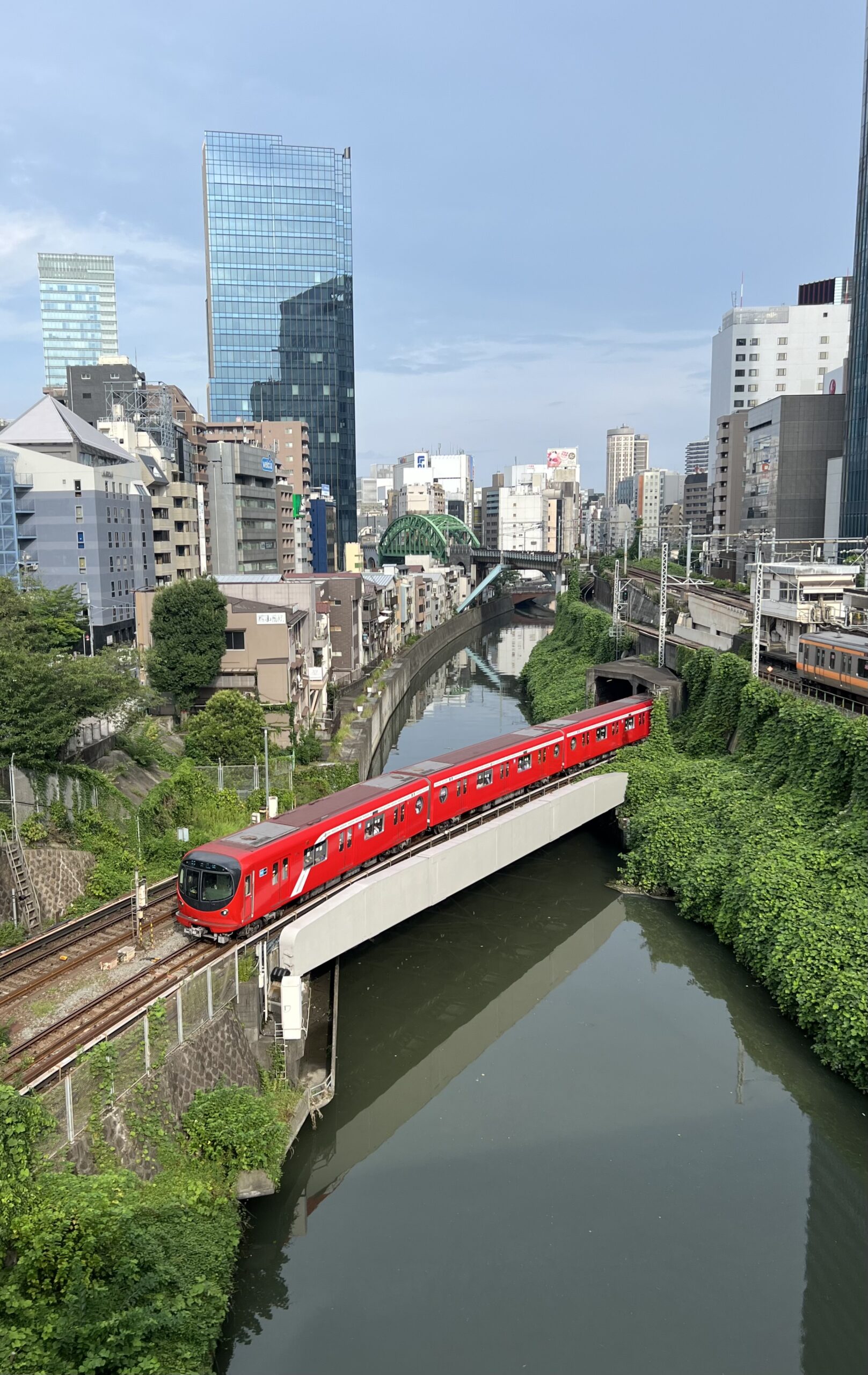 Red commuter train crossing a bridge over the Kanda River surrounded by urban buildings in central Tokyo, Japan.